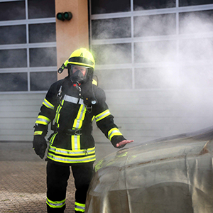 Feuerwehrmann hält Hand über brennendes E-Auto mit Jutec Brandbegrenzungsdecke